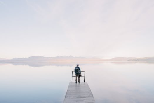 A solitary traveler stands on a dock enjoying the serene water view